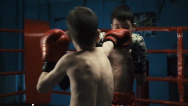 Two shirtless boys wearing gloves and fighting on ring practicing Thai box looking serious and determined.