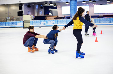 Group of teenage friends ice skating on an ice rink - obrazy, fototapety, plakaty
