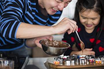 Obraz na płótnie Canvas 女の子とパパがお菓子を作っている。チョコレートを型に落としている。