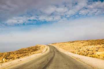Naklejka premium The road in the desert with yellow sand and clouds on the sky