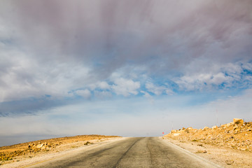 The road in the desert with yellow sand and clouds on the sky