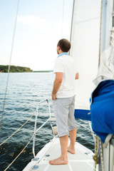 Handsome young man standing alone on yacht or sailboat in sea, copy space. Sailing, tourism, travel and people concept