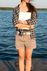 Creative young brunette woman with sketchbook and pencils in hand standing on pier. Vacation, traveling and freedom concept