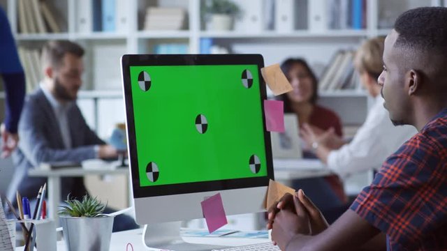 Tracking shot shot of young black man watching something on green computer screen with sticky notes attached to it and talking