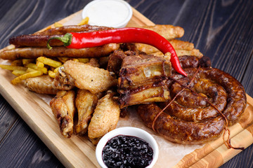 Mixed fresh grilled meat and sausage with pepper, french fries and sauce on wooden cutting board. Assorted meat with vegetables from summer BBQ. Healthy eating. Delicious barbecued ribs