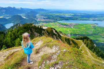 Cute little hiker enjoying picturesque views from the Tegelberg mountain, a part of Ammergau Alps, located nead Fussen town, Germany.