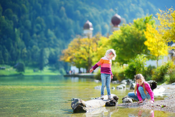 Adorable sisters playing by Konigssee lake in Germany on warm summer day. Cute children having fun...