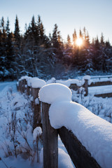 Snow covered wooden fence on a cold winter's day with the sun setting behind the forest