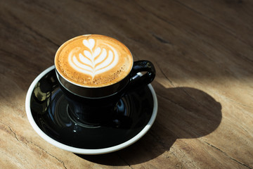 Close up hot black coffee cup with tree heart shape latte art milk foam on wood table near window...