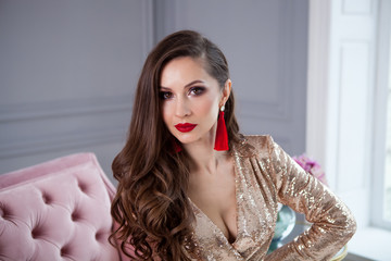 Close up fashion stile portrait of pretty girl in stylish gold shining party dress sits on a pink...