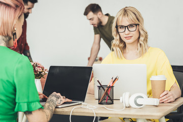 selective focus of young blogger in eyeglasses sitting at workplace and creative workers in office