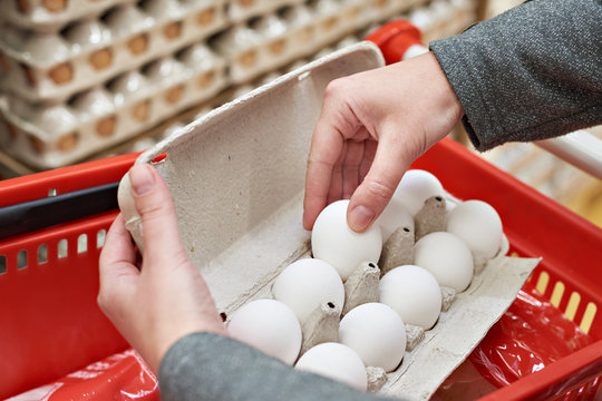 Hands with packages of white eggs in store