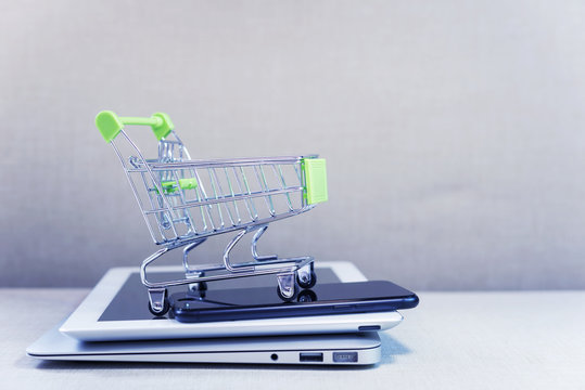 Online business and e-commerce or shopping online concept. Shopping basket on top of stack of laptop, tablet and mobile phone. Wireless technology for business with free copy space.