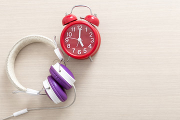 Red alarm clock and headphone on wood table with free copy space for text. Education and music concept.