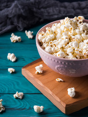 Popcorn in pink bowl on wooden board on dark green background