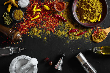 Cooking using fresh ground spices with mortar and small bowls of spice on a black table with powder spillage on its surface, overhead view with copyspace