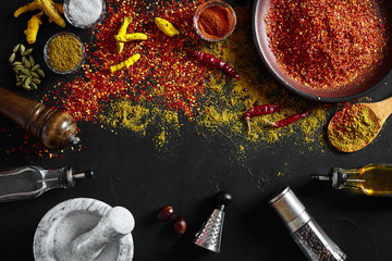 Cooking using fresh ground spices with mortar and small bowls of spice on a black table with powder spillage on its surface, overhead view with copyspace