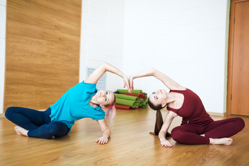 Two women in sportswear doing stretching exercises on yoga mat. Healthy living and fitness concept