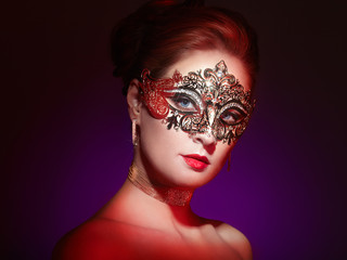 Beautiful Woman Wearing Venetian Masquerade Carnival Mask at Party, over Colorful Background. Christmas and New Year Celebration. Sexy Girl with Holiday Makeup and Red lips. Golden Mask