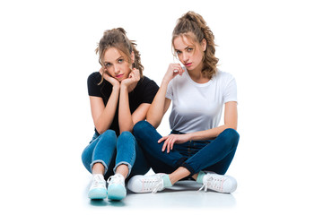 attractive young twins sitting on floor and looking at camera on white