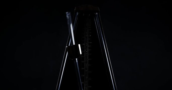 Slow motion shot of vintage metronome with golden pendulum beats slow rhythm on the dark background
