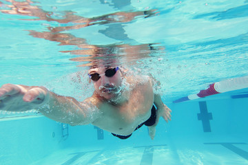 A professional swimmer trains with effort and dedication to win the race by swimming in a freestyle pool. Concept of: sport, swimming pool, competition, fitness.