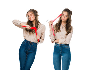 happy and bored twins with hangers looking at camera isolated on white, shopping concept