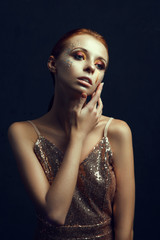 Beautiful model wearing golden dress is posing in a dark studio 