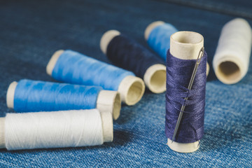 Fototapeta na wymiar Spools of white and blue threads and sewing needle on denim