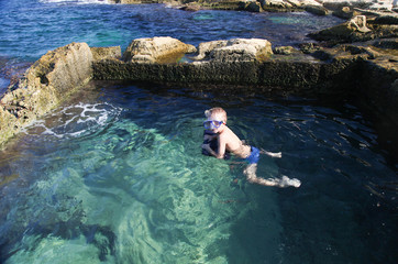 Small boy swimming in natural stone pool in the sea. Malta. Horizontal view.