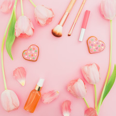 Frame with tulips flowers and cosmetics, cookies on pink pastel background. Flat lay, top view. Spring time background.