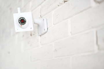 White web surveillance camera on a white brick wall. Security technologies.