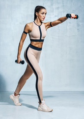 Slender latin girl in fashionable sportswear holding dumbbells. Photo of muscular fitness model on...