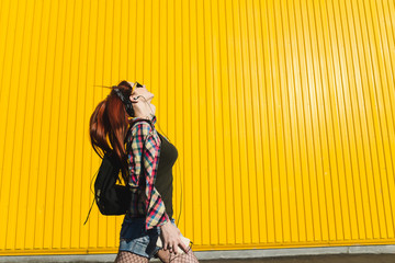 Redhead girl in denim shorts and pantyhose mesh is listening music with headphones on yellow background