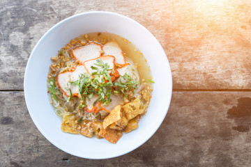 Close-up of Thai Noodle Soup with Meat in white bowl on wooden background.
