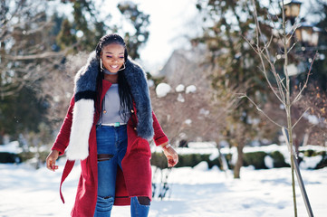 Rich african american girl in red coat and fur on winter street at sunny weather. Black stylish woman.