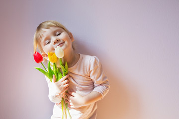 Sweet happy little blond-haired girl holding a bouquet of colorful tulips in her hands. Shot 3/4. Copy space.