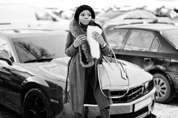 Rich african american girl in red coat and fur against red muscle car. Black stylish successful businesswoman.