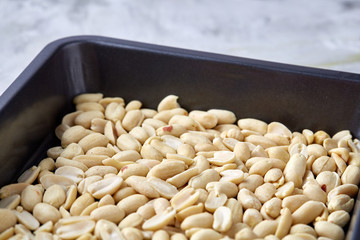 Peeled peanut on baking tray over white textured background, selective focus, shallow depth of field.