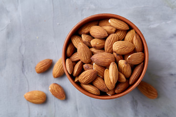 Bowl of almonds on white textured background, top view, close-up, selective focus.