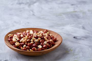 Raw mixed peanuts in wooden plate isolated over white textured background, top view, close-up.