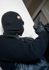 Armed man in balaclava hiding behind a wall.