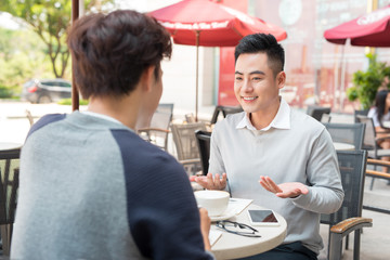 Two young handsome businessmen in casual clothes smiling, talking in coffee shop.