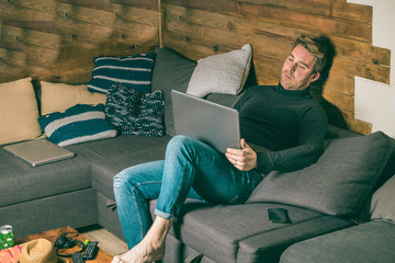 Guy on the couch at home looking at the computer. Blond boy in casual dress