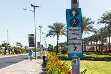 Button for calling the pedestrian crossing with the up arrow. click here to cross it written in four languages English, Arabic, Russian and German
