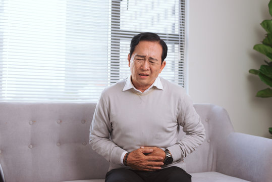 Senior Asian Man With .stomach Ache While Sitting On Sofa