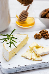 Cheese plate served with crackers, honey and nuts. Camembert on white wood serving board over white texture background. Appetizer theme.