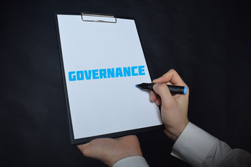 In the hands of a businessman a notebook with the inscription:GOVERNANCE