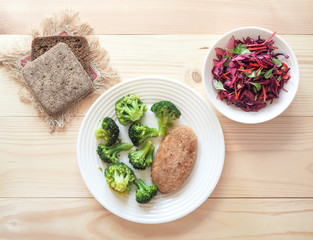 Cutlet and broccoli on white plate on light wooden background.