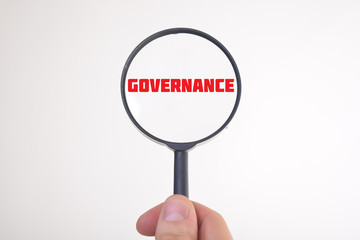 Businessman looking at a magnifying glass word:GOVERNANCE